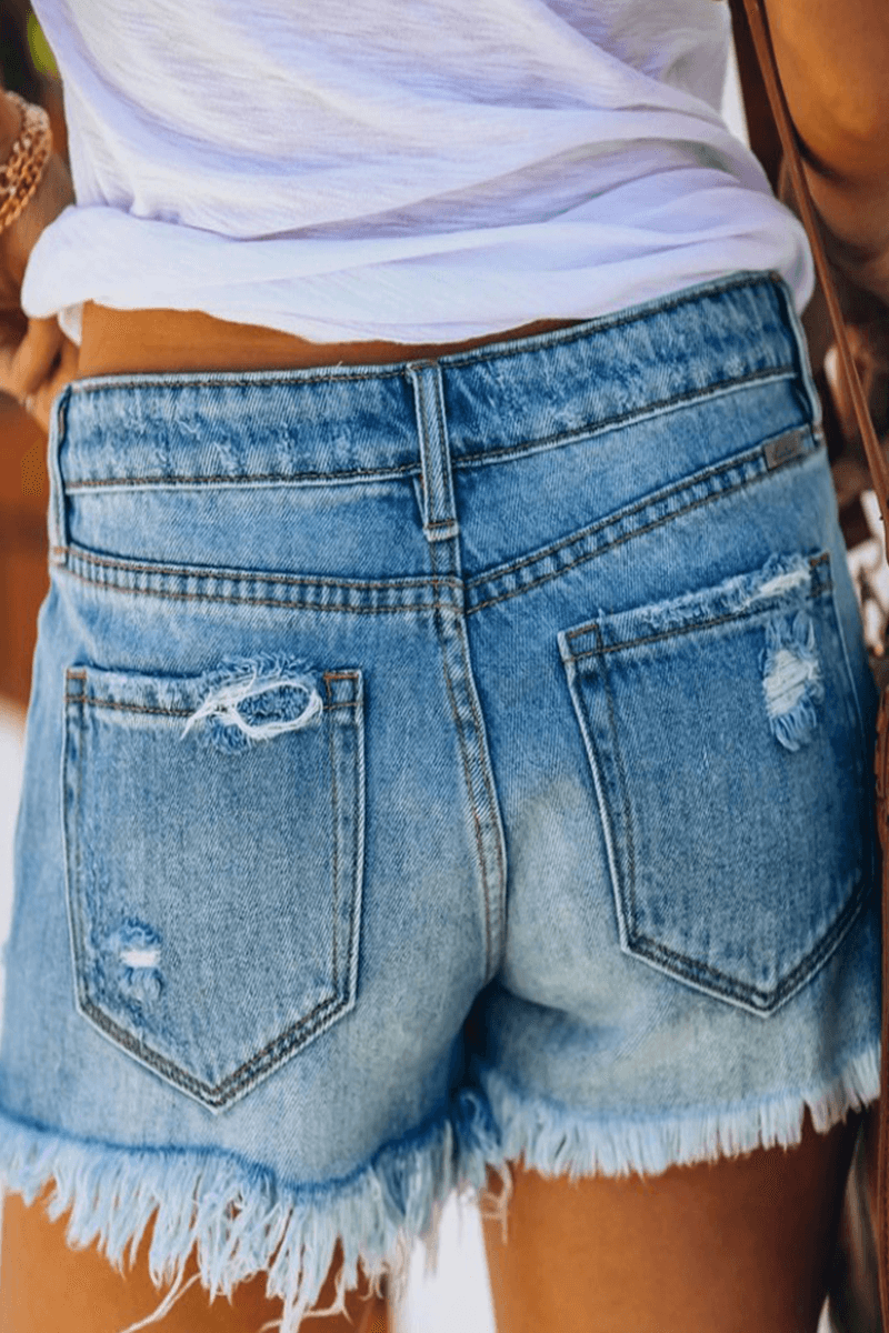 Women's high-waisted distressed blue jean shorts with fringe. Perfect casual denim shorts for trendy summer fashion.