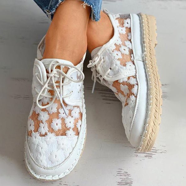 Close-up of women's white fashion sneakers, featuring intricate floral embroidery & comfortable mesh.
