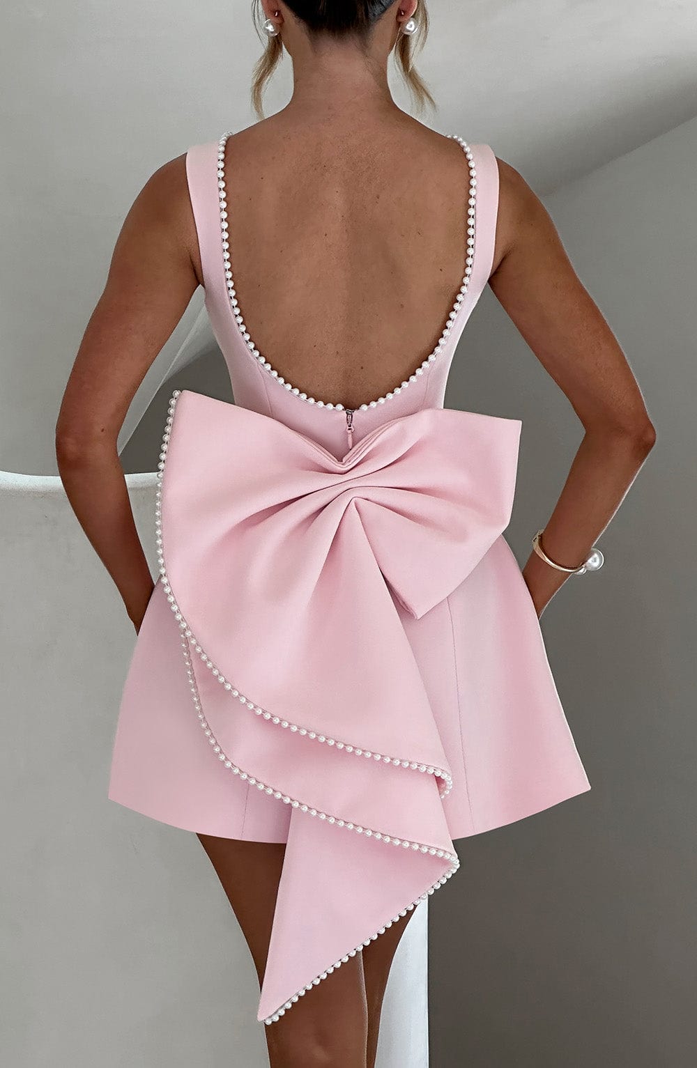 Chic women's party mini dress featuring a stylish bow back and delicate pearl trim detail.