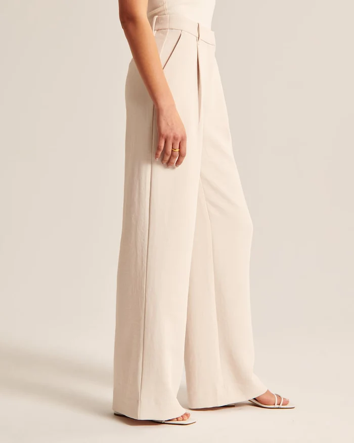Model wearing women's beige wide-leg tailored trousers, high-waist, elegant style for both formal and casual occasions.