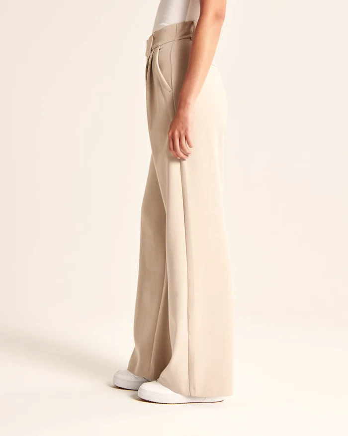 Model wearing women's beige wide-leg tailored trousers, high-waist, elegant style for both formal and casual occasions.