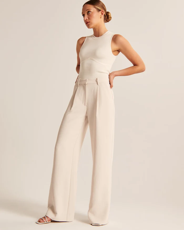 Model wearing women's beige wide-leg tailored trousers, high-waist, elegant style for both formal and casual occasions.
