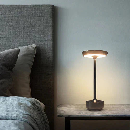 Gold design table lamp, USB rechargeable, providing warm ambient light for a cozy bedroom.