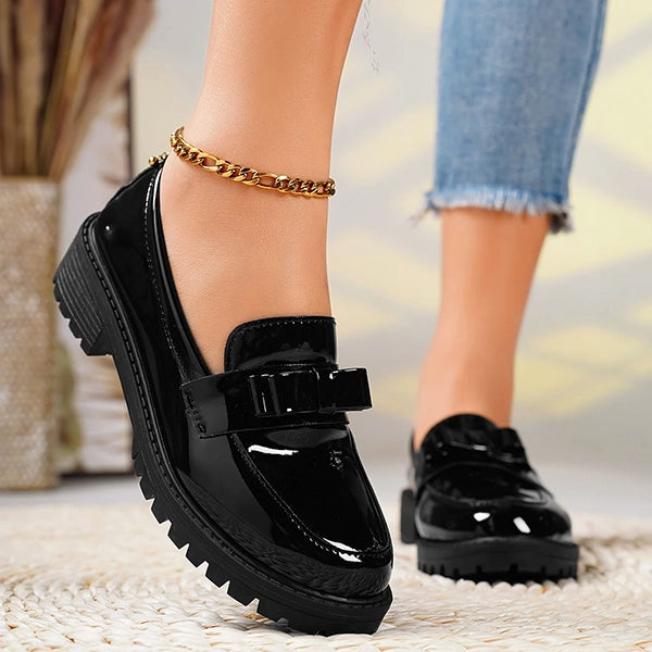 Women's black slip-on platform loafers with a chic bow detail, glossy finish, and comfortable lug sole.