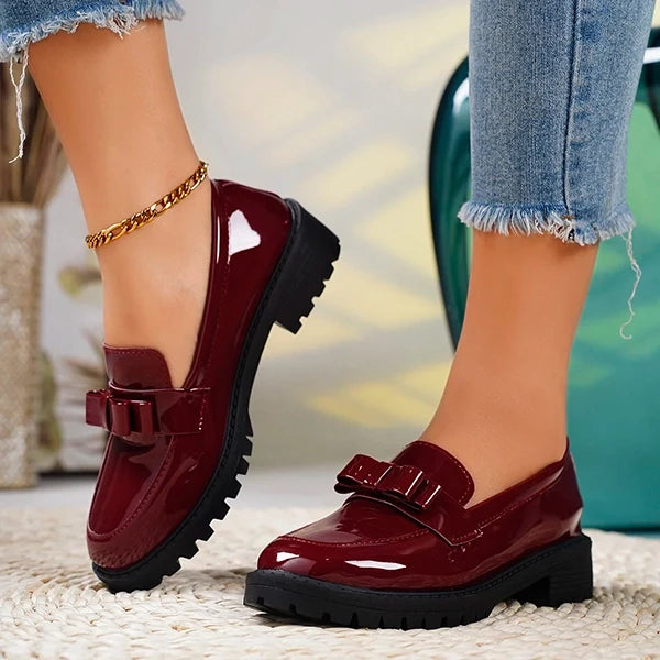 Close-up of women's glossy platform loafers, highlighting the chic bow, slip-on design, and sturdy lug sole.