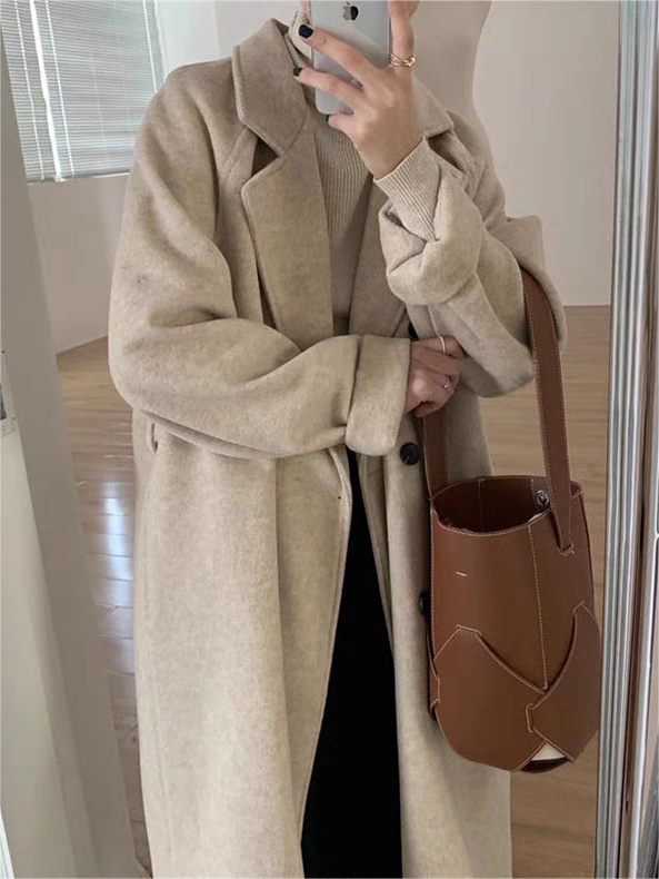 Back view of a women's oversized long winter coat with a belted waist, emphasizing its soft texture and graceful drape.