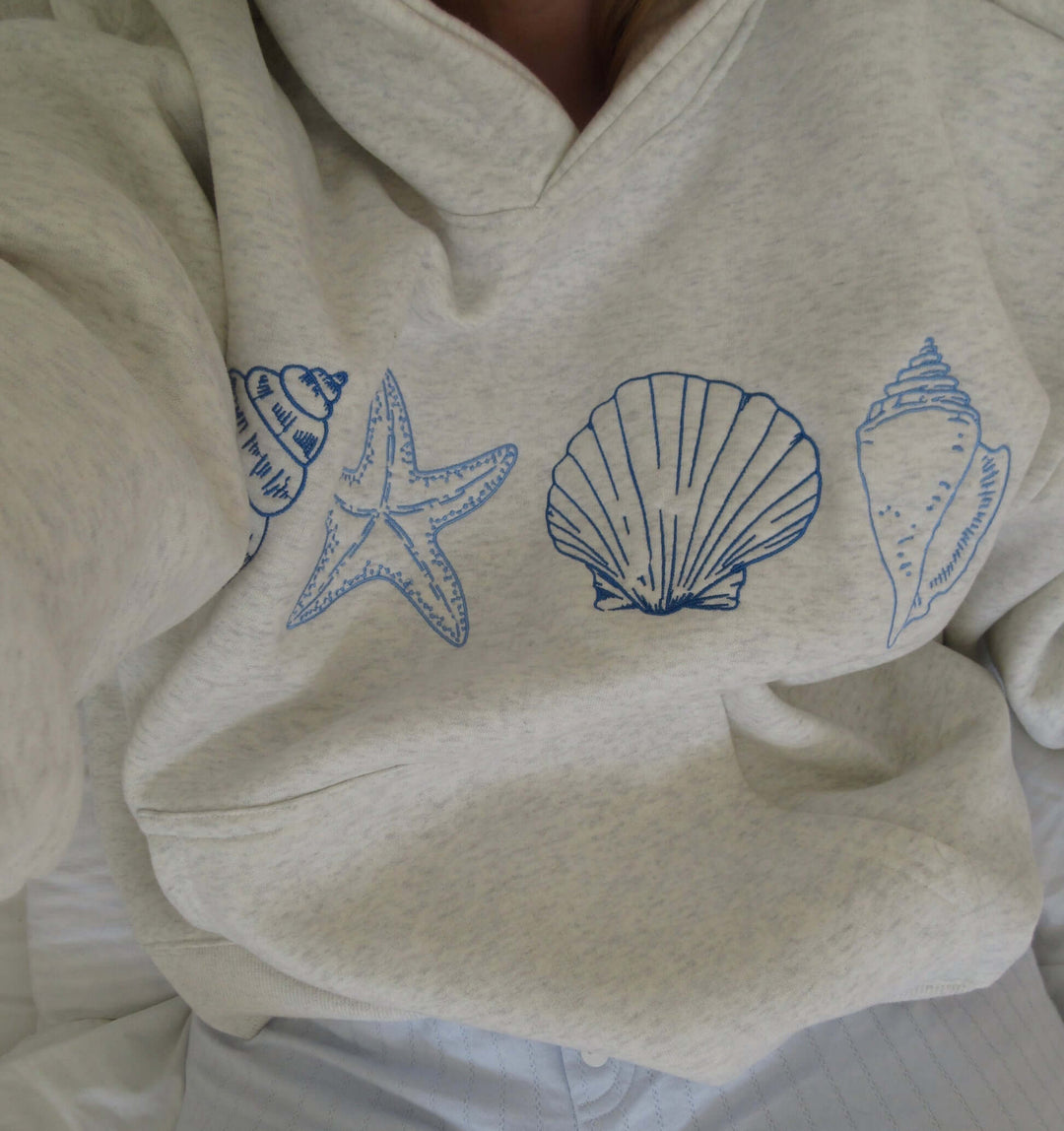 Women's grey hoodie with elegant seashell print, offering coastal comfort. Perfect relaxed fit for casual beach style.