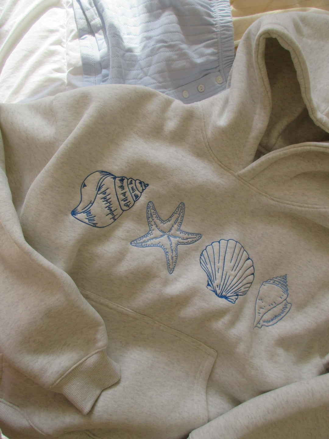 Coastal style women's hoodie featuring a unique seashell print. Comfortable grey beachwear top with a relaxed fit.