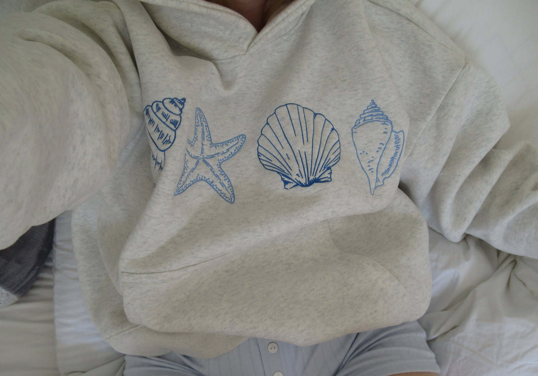 Relaxed fit women's grey hoodie showcasing a detailed seashell print. Ideal comfortable casual top for beach or everyday.