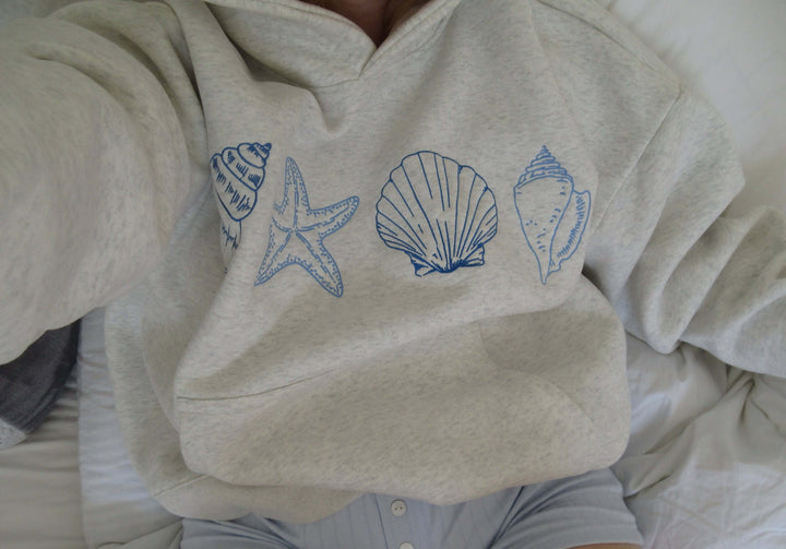 Relaxed fit women's grey hoodie showcasing a detailed seashell print. Ideal comfortable casual top for beach or everyday.