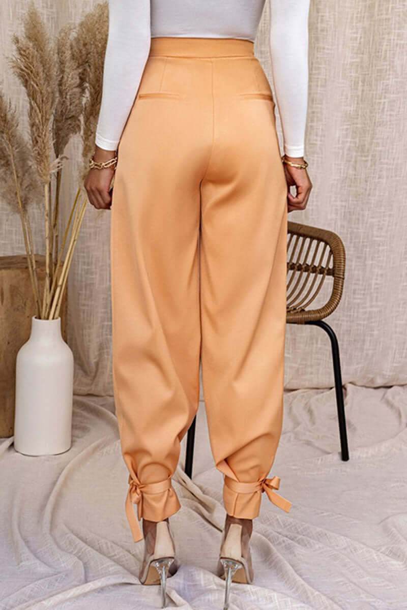 Woman modeling high-waisted tapered trousers with ankle ties, showcasing modern office and casual styles.