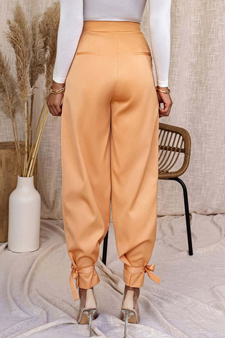 Woman modeling high-waisted tapered trousers with ankle ties, showcasing modern office and casual styles.