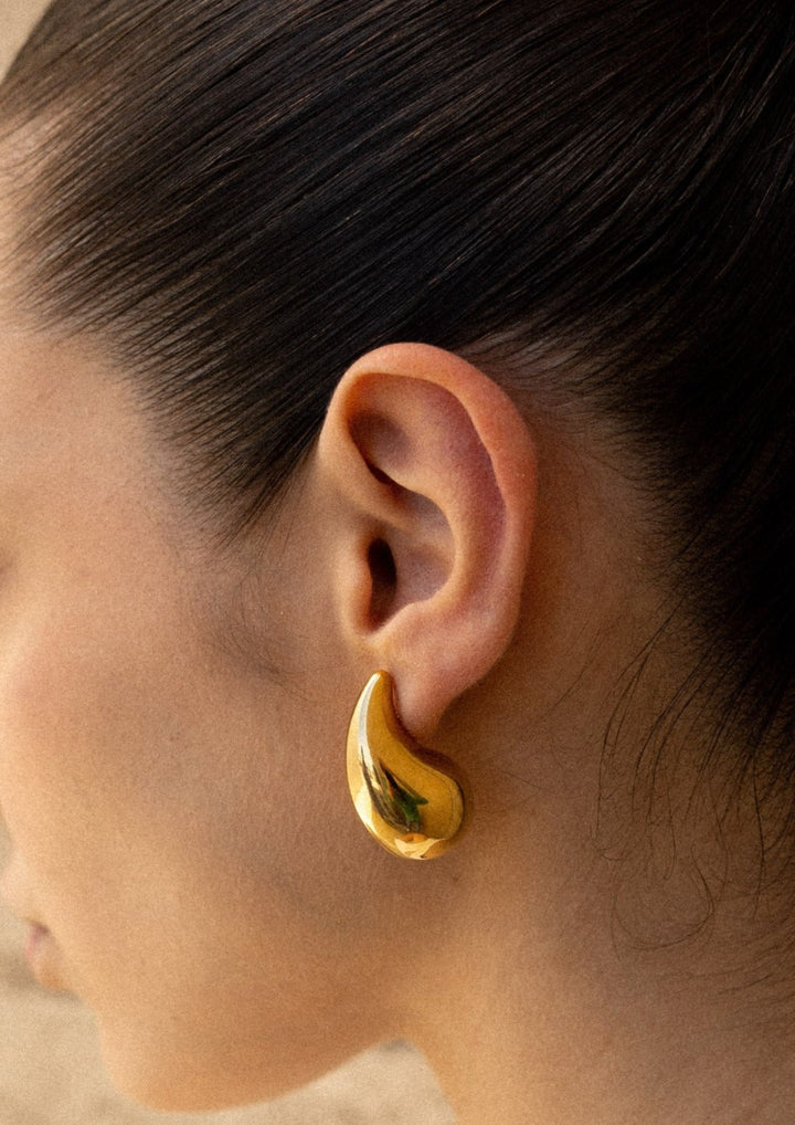 Woman wearing elegant polished teardrop dangle earrings, chic stainless steel jewelry for any occasion.