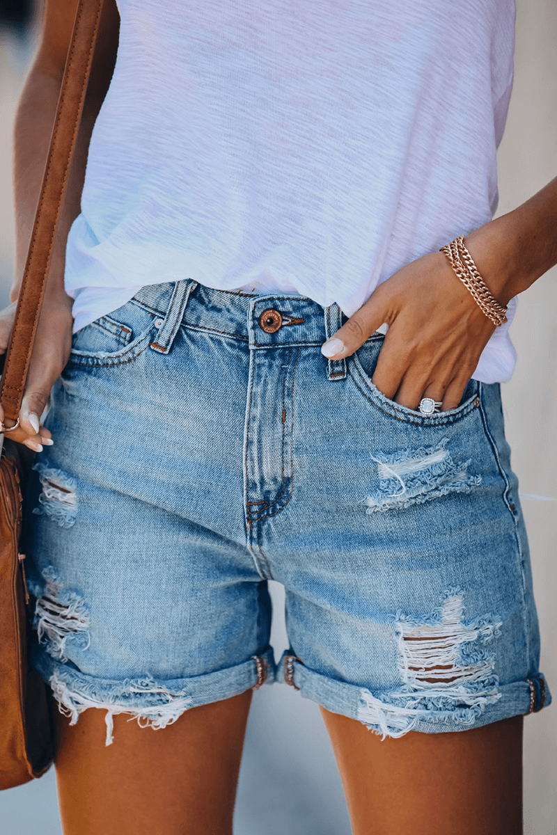 Close-up of trendy women's distressed denim shorts featuring rips and fashionable fringes.
