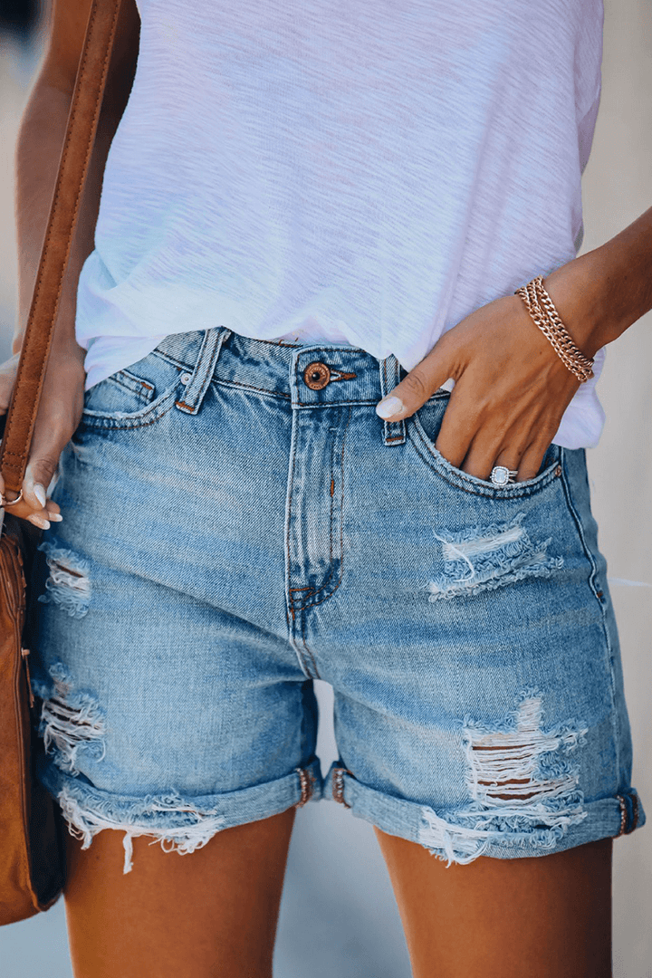 Close-up of trendy women's distressed denim shorts featuring rips and fashionable fringes.