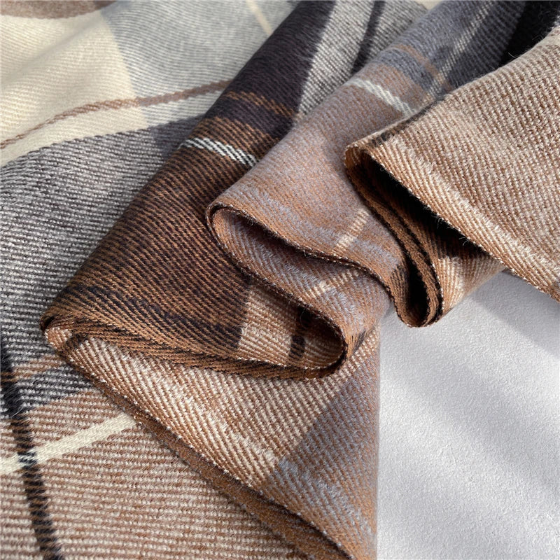 Close-up of a women's knitted cashmere-feel scarf, showing detailed checkered pattern & tassels.